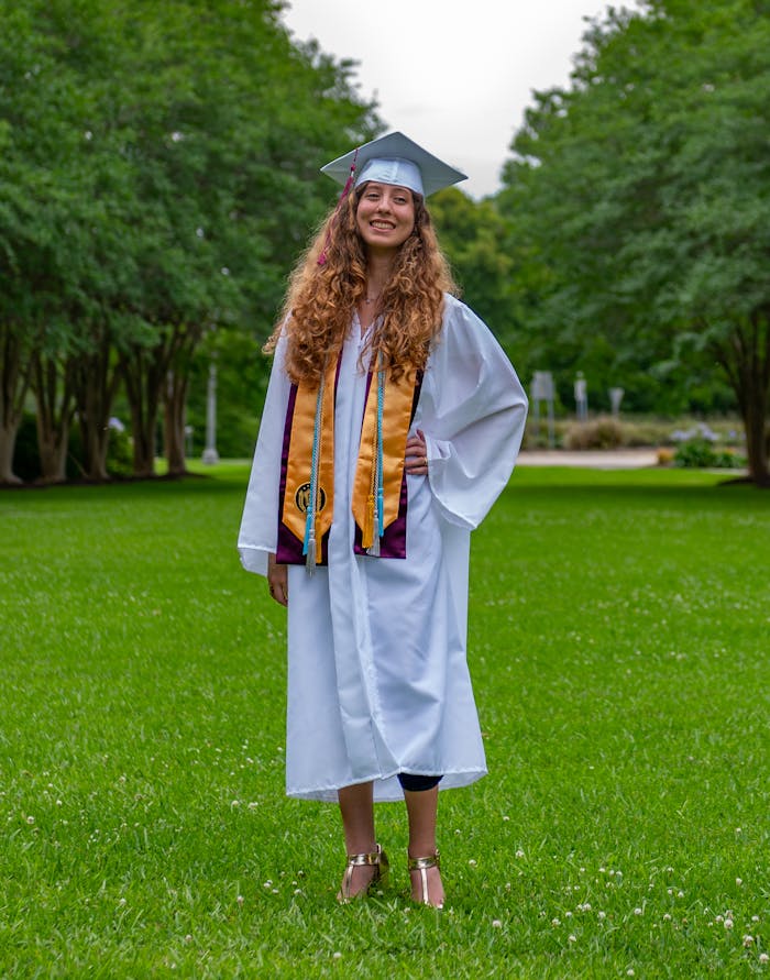A happy young woman in cap and gown celebrating her graduation outdoors.